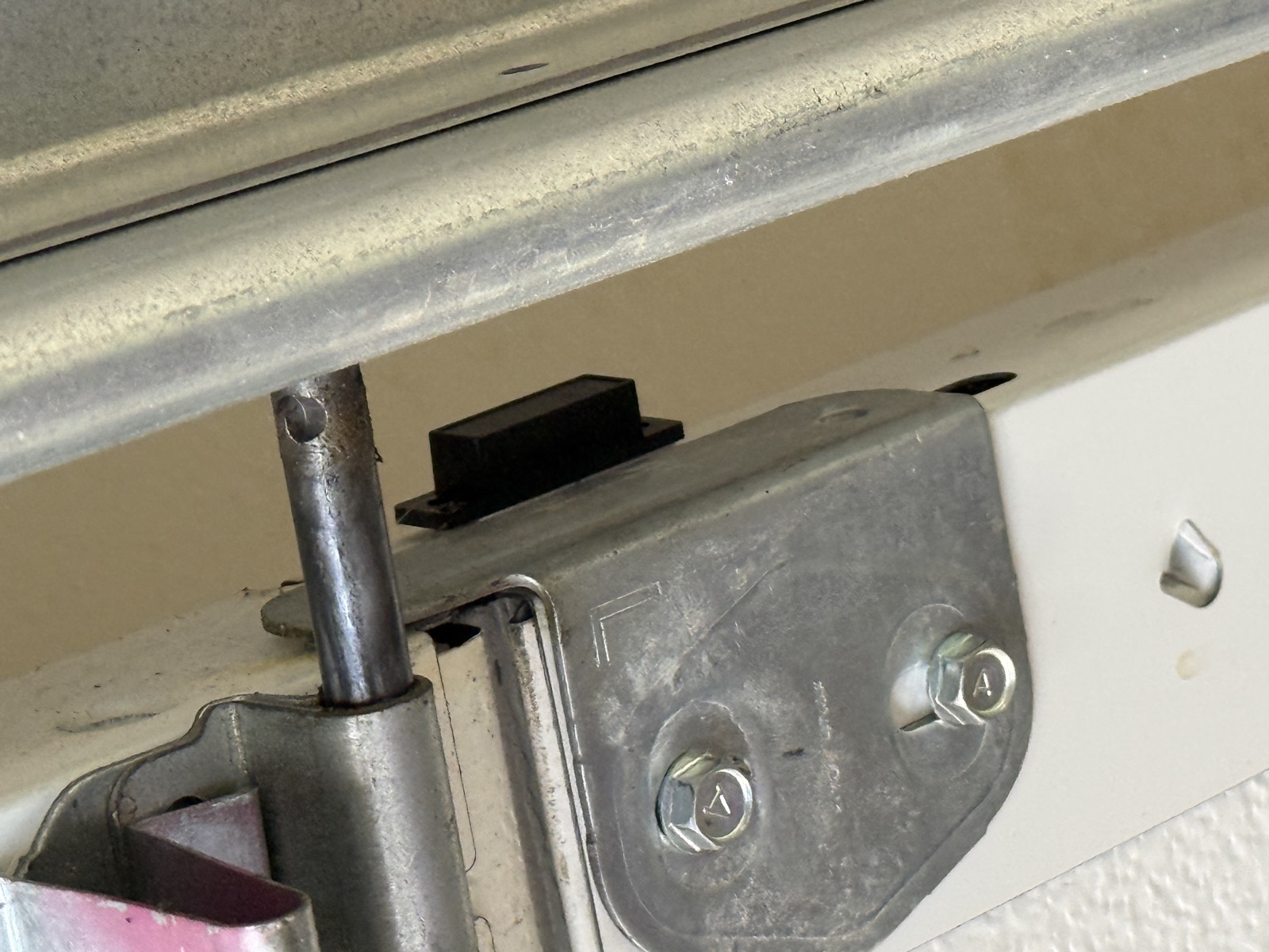 A close-up of the reed sensor mounted on the top section of the garage door, sitting just below the horizontal track with its bracket bolted to the door's steel angle.